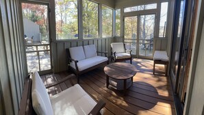 Une terrasse couverte avec une plateforme en bois, des sièges blancs rembourrés et un ventilateur de plafond.