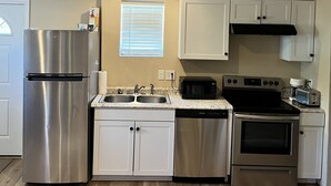 A modern kitchen with stainless steel appliances, white cabinetry, and a wooden floor. - Small Cozy Quite House (Wylie)