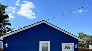 A blue single-story building with a white door and window, a small porch area, and a concrete driveway. - Small Cozy Quite House (Wylie)