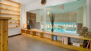 A reception area with a reception desk, a large window with a view of a pool, and shelves with books and decorative items. - Studio Apartment "Schmetterling" Near the Slopes with Shared Pool and Wi-Fi (Sankt Englmar)