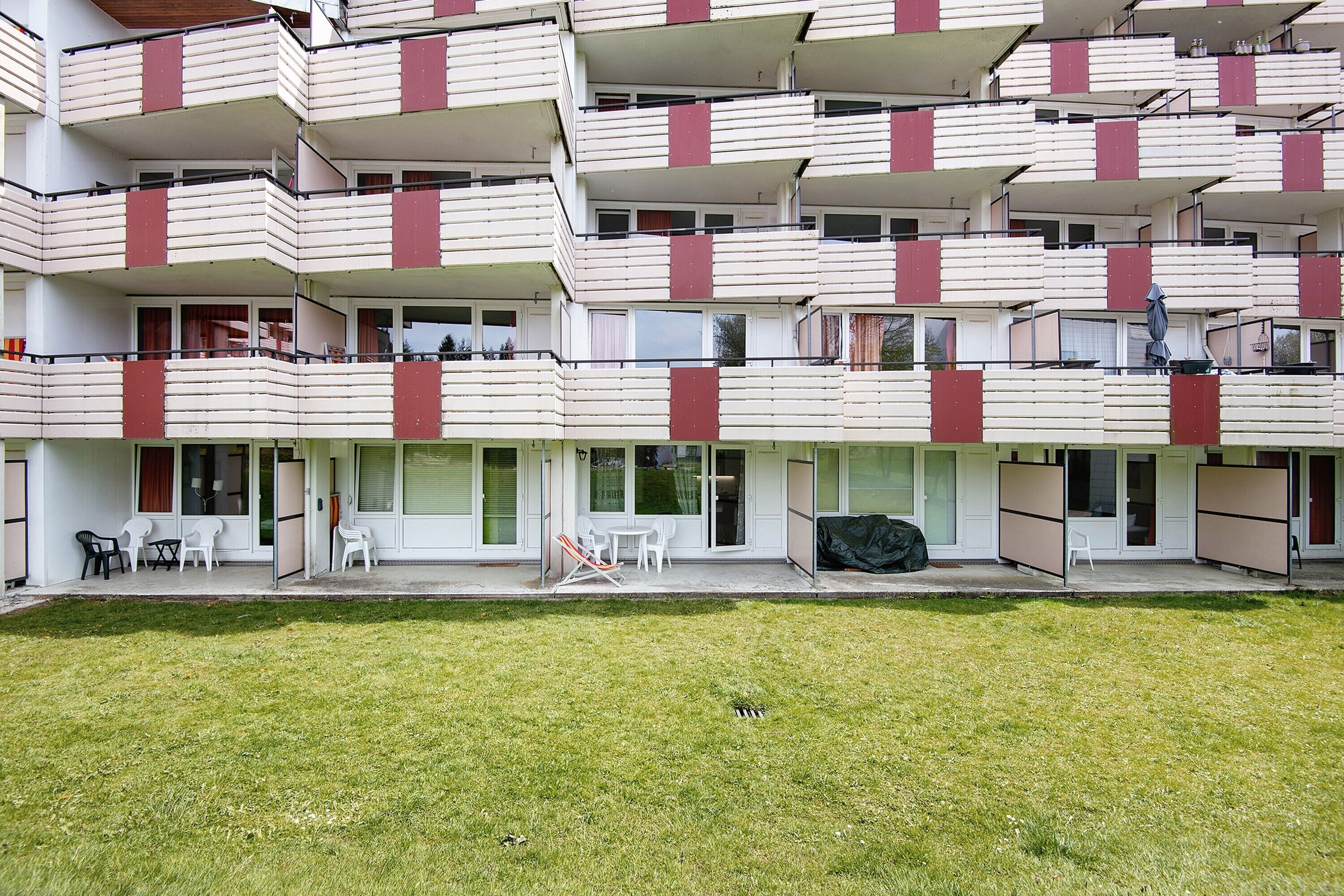 A multi-story residential building with balconies, a lawn, and outdoor seating.