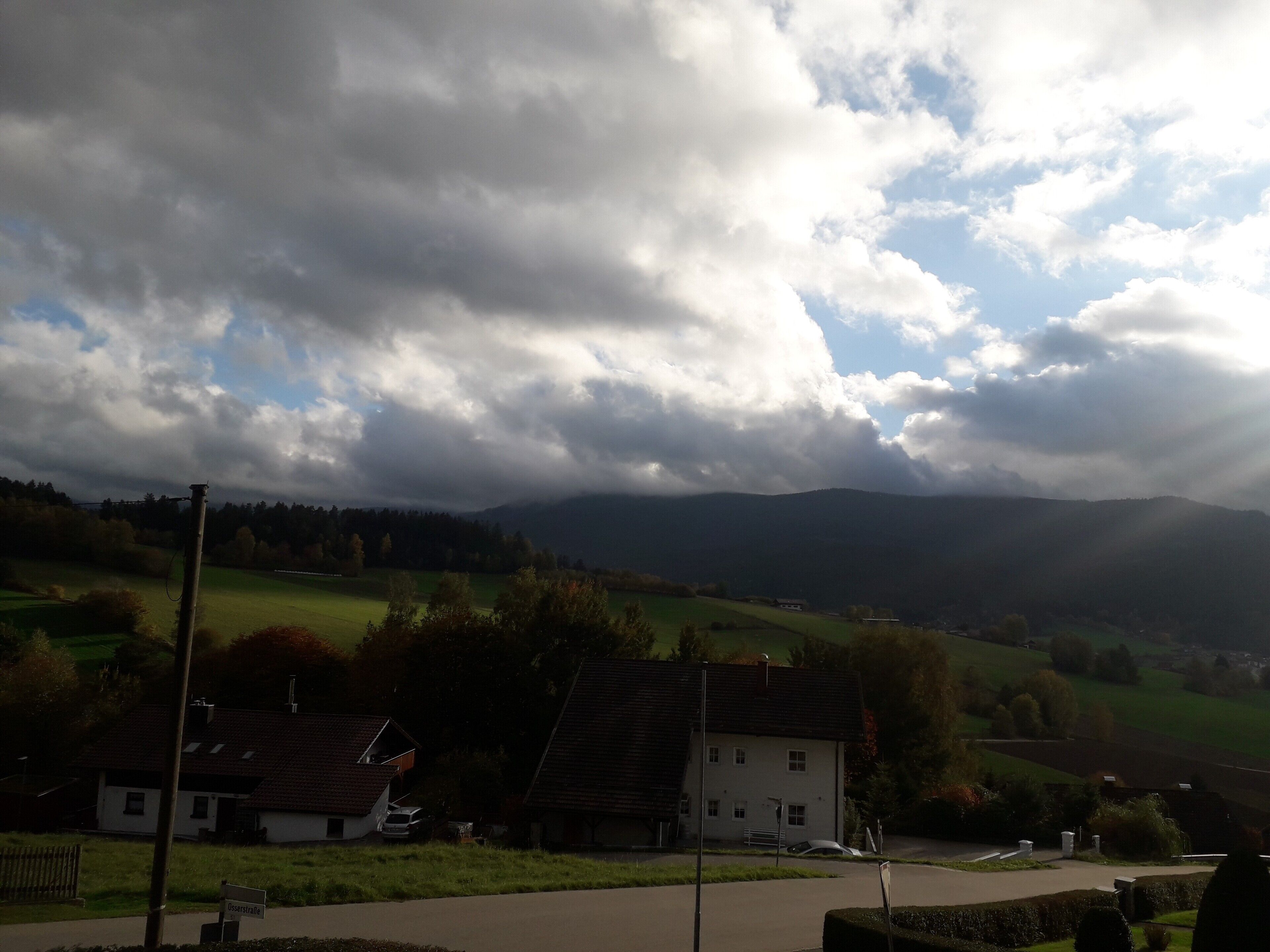 A rural landscape with houses, a road, and a sign reading 'Ossersstraße.'