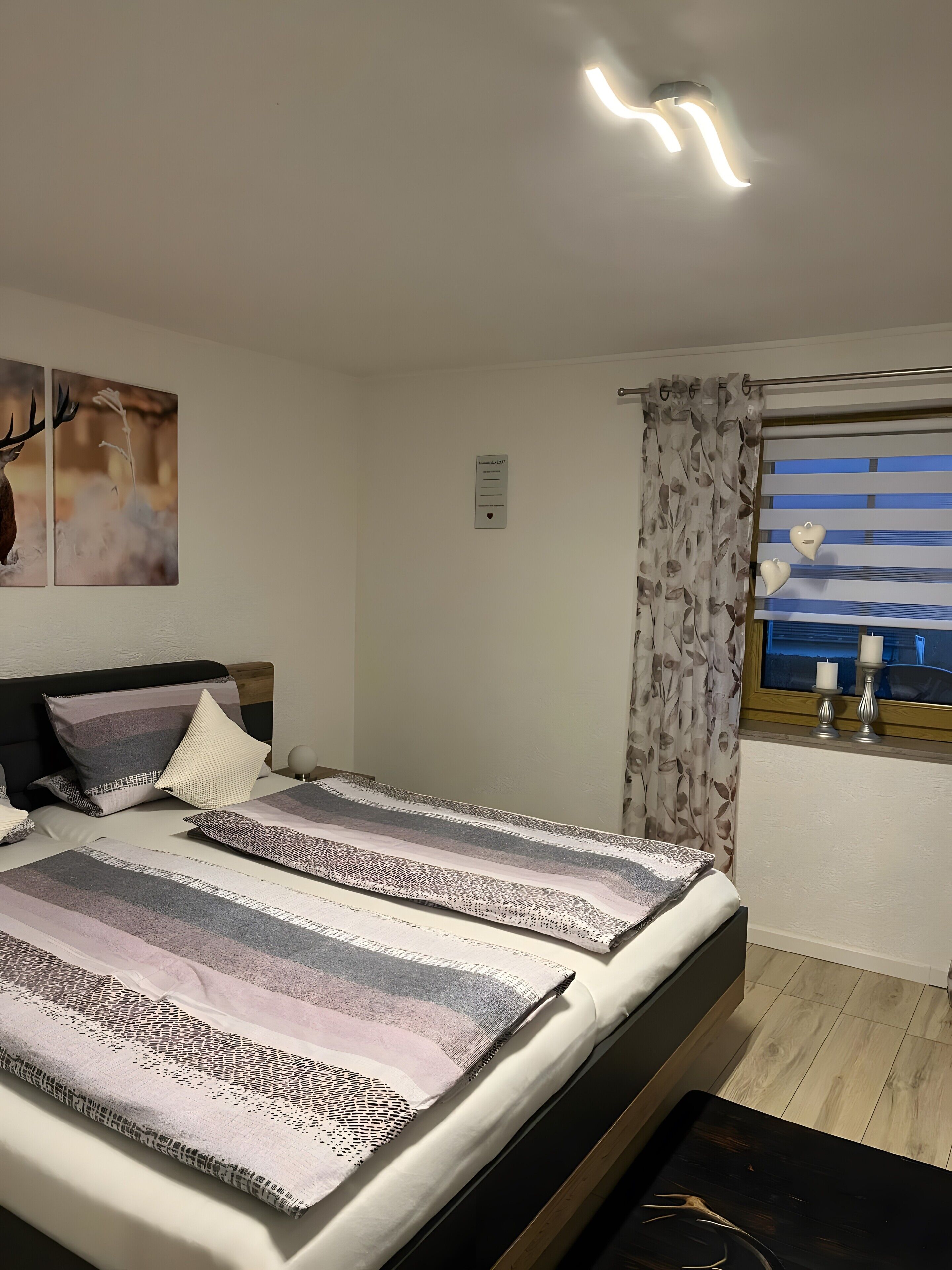 Una camera da letto con un letto, una testata, una finestra con tende e opere d'arte appese al muro.