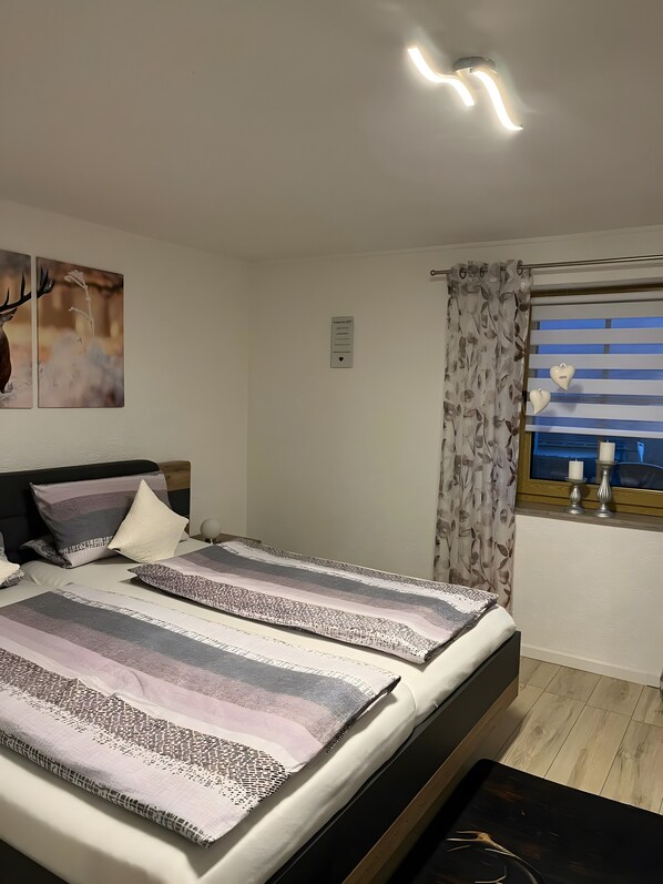 Un dormitorio con cama, cabecera, ventana con cortinas y una obra de arte en la pared.