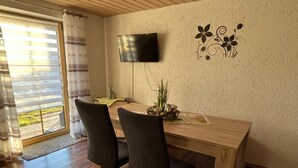 A dining area with a wooden table, two chairs, a flat-screen TV mounted on the wall, and a decorative wall piece. - Holiday Apartment "Ferienwohnung Köppl" with Terrace (LAM)