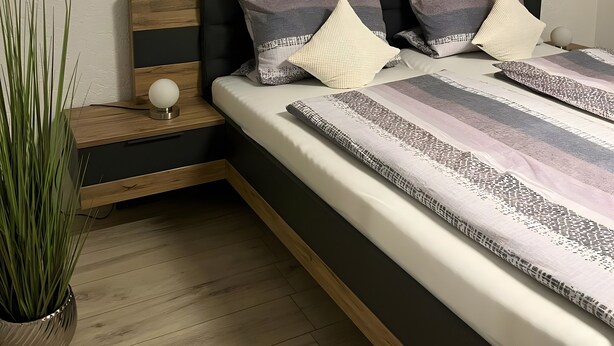 Een slaapkamer met een bed, een nachtkastje, een potplant en twee schilderijen van herten.
