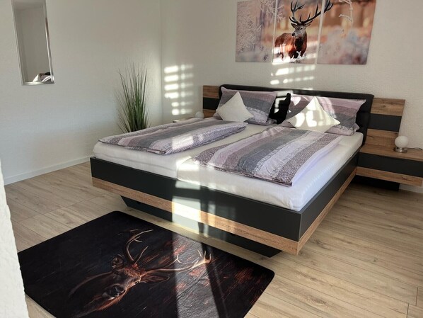 A modern bedroom with a large bed, a bedside table, a mirror, and a wall-mounted artwork.