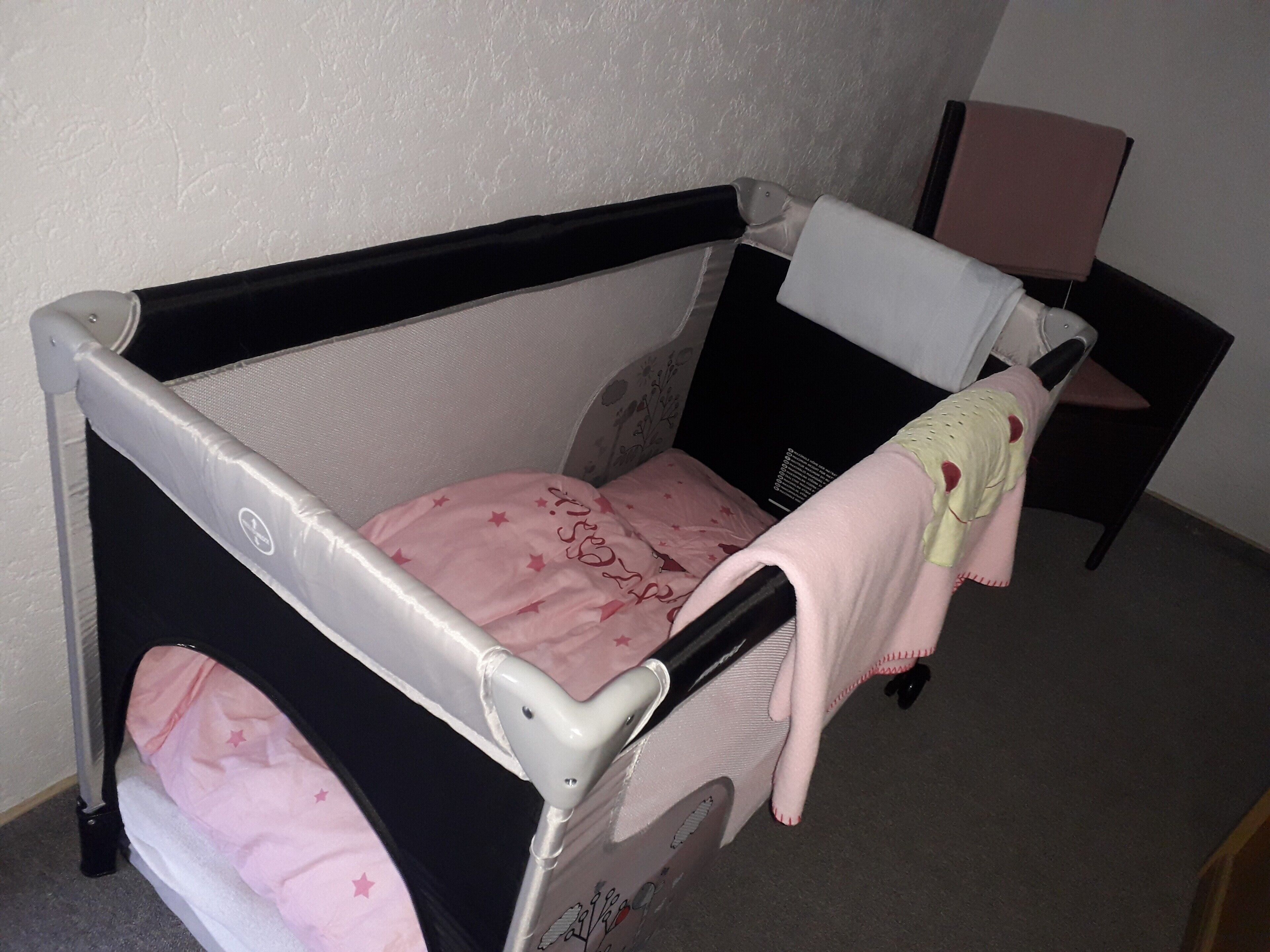 Um berço infantil com tela lateral, colchão rosa e um cobertor.