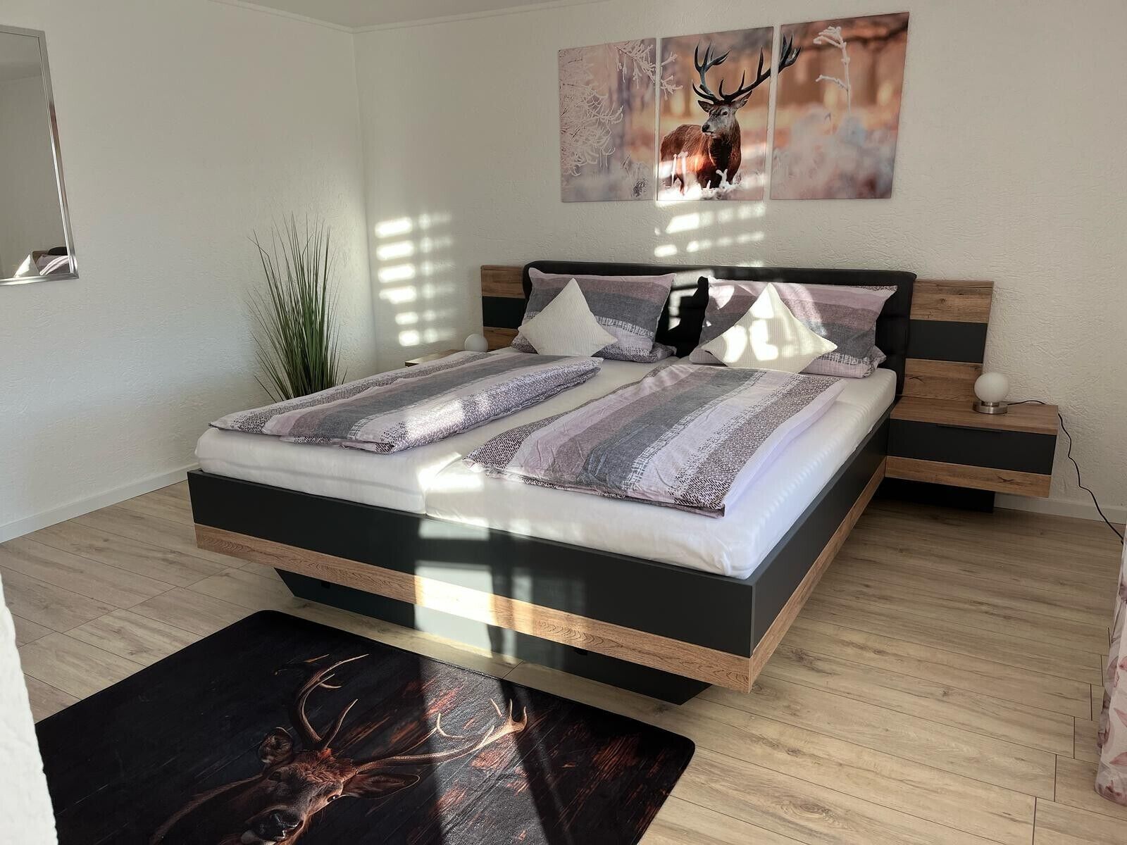Ein modernes Schlafzimmer mit Bett, Nachttischen, Spiegel und einem Wandbild.