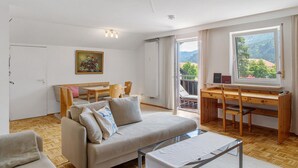 A modern living room with a sofa, a wooden desk, and a dining area. - Holiday Apartment "Anette" with Mountain View, Balcony & Wi-Fi (Garmisch-Partenkirchen)