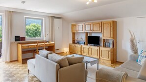 A modern living room with a wooden desk, sofa, and television. - Holiday Apartment "Anette" with Mountain View, Balcony & Wi-Fi (Garmisch-Partenkirchen)