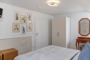 Ein Schlafzimmer mit Bett, Kleiderschrank, Schminktisch und Spiegel, sowie gerahmten Pflanzenbildern an der Wand.