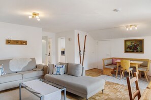 Ein Wohnzimmer mit einer Couch, einem Glastisch, einer Holzbank und einem Esstisch mit Stühlen.
