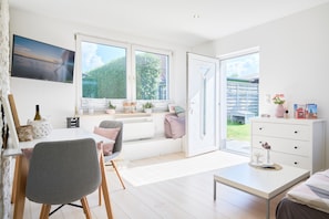 Una habitación luminosa con un ventanal grande, zona de comedor, sofá y cómoda blanca.