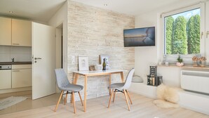 Une cuisine moderne avec des armoires blanches, un coin repas avec deux chaises, un mur décoratif en briques et une grande fenêtre donnant sur les arbres.