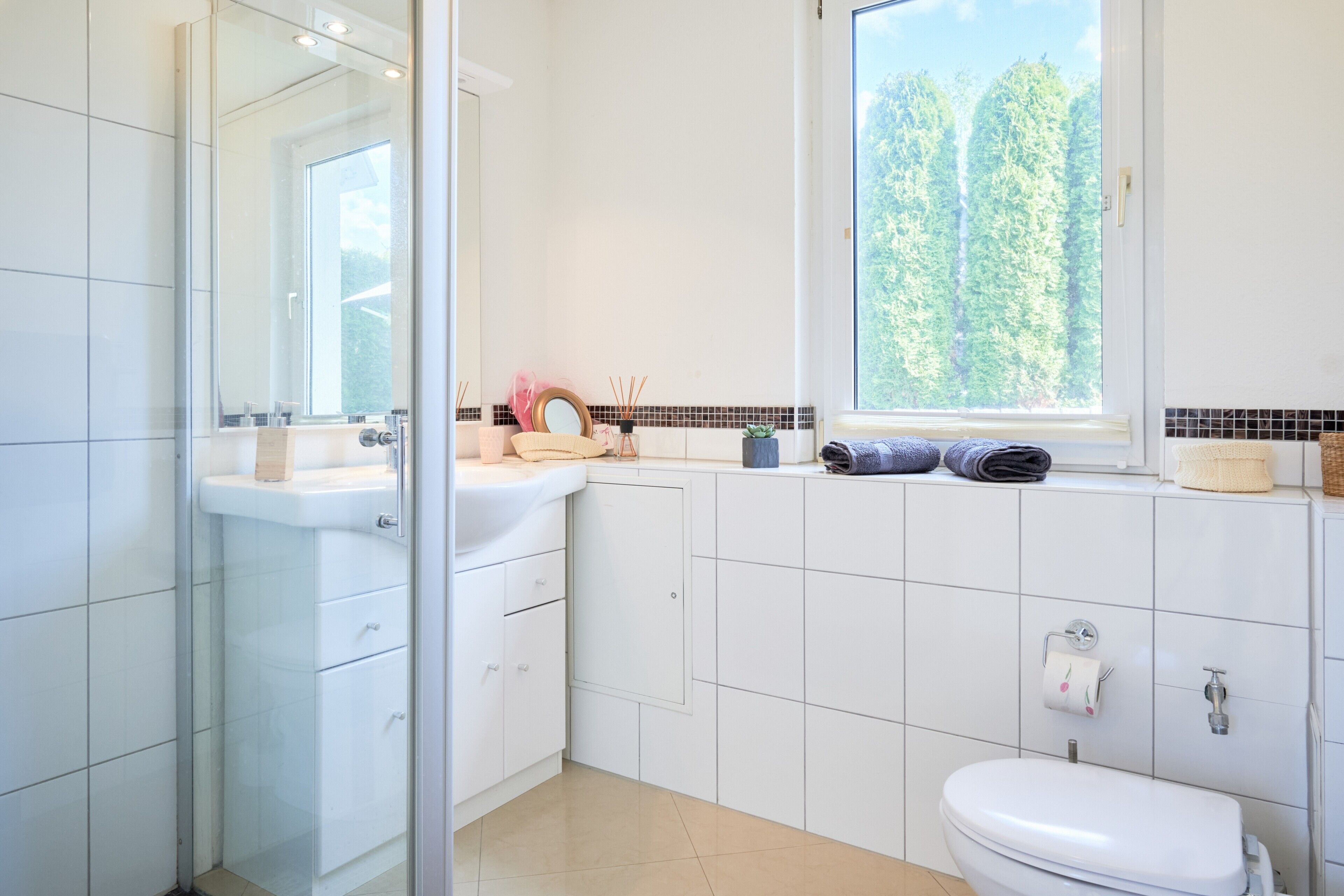 A modern bathroom with a glass shower enclosure, a sink with a mirror, a toilet, and a window with a view of trees.