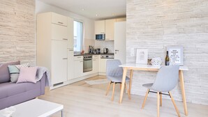 Une cuisine moderne avec des meubles blancs, un four à micro-ondes et un coin repas comprenant deux chaises et une table.