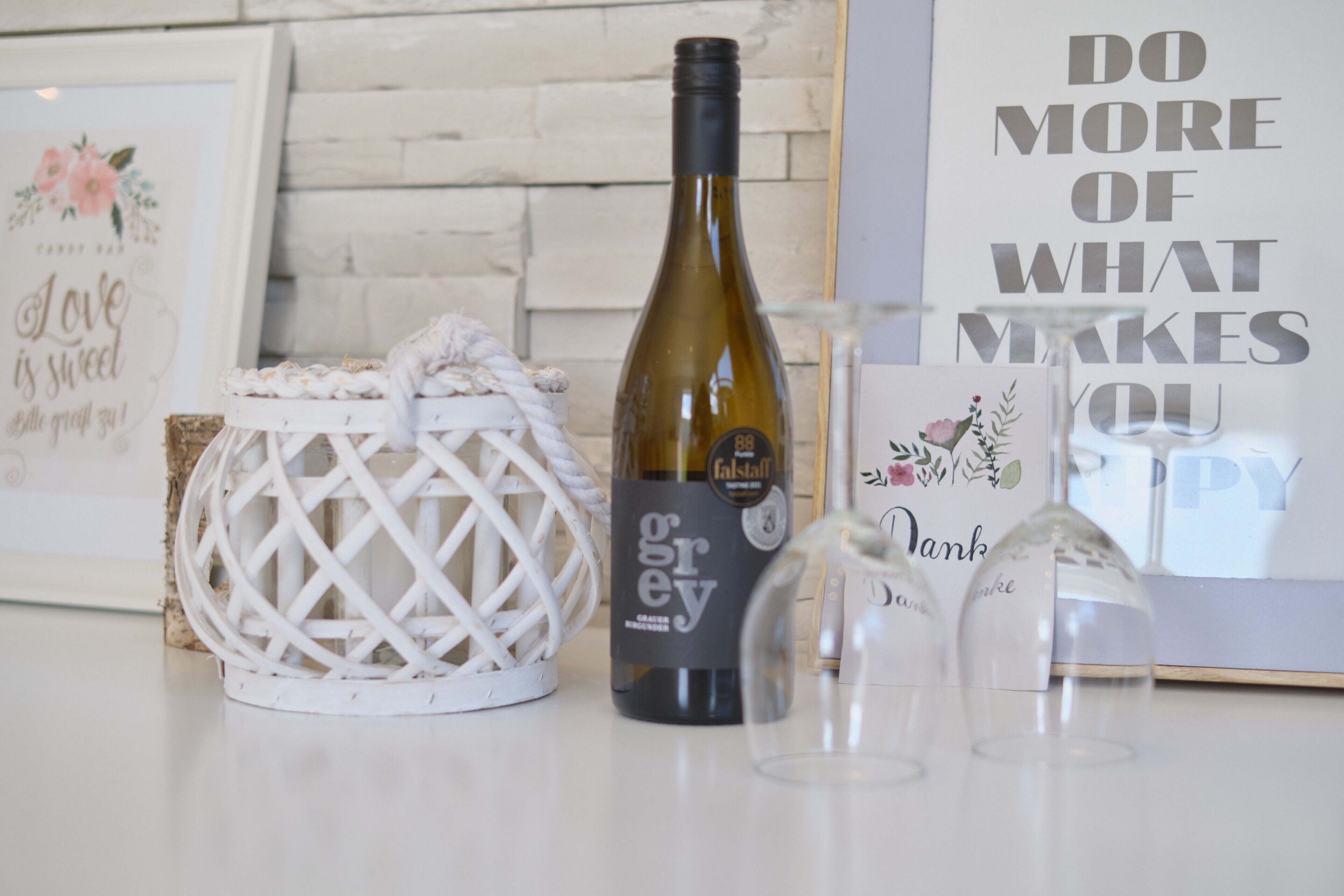 Une bouteille de vin, un panier décoratif et une citation inspirante encadrée, le tout posé sur une table.