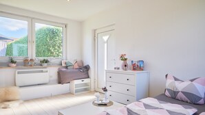 Une chambre avec un coin fenêtre, une commode, un lit et un radiateur.