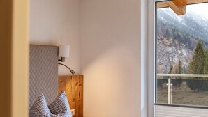 Une chambre à coucher avec un lit, une table de chevet, une lampe et une fenêtre donnant sur les montagnes.