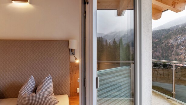 Une chambre avec un lit, des oreillers, une lampe et une vue sur un paysage montagneux, visible à travers une porte vitrée.