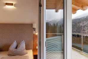 Una habitación con cama, almohadas, una lámpara y vistas a un paisaje montañoso a través de un ventanal.