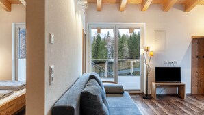Un salon moderne avec un canapé, un téléviseur posé sur un meuble en bois et une grande fenêtre donnant sur des arbres et un escalier.