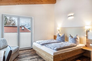 A bedroom with a wooden bed, checkered pillows, a bench, and a view of a building through a sliding door.