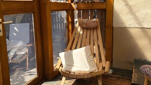 Ein Schaukelstuhl aus Holz mit Kissen, ein Holzboden und Blick ins Freie.