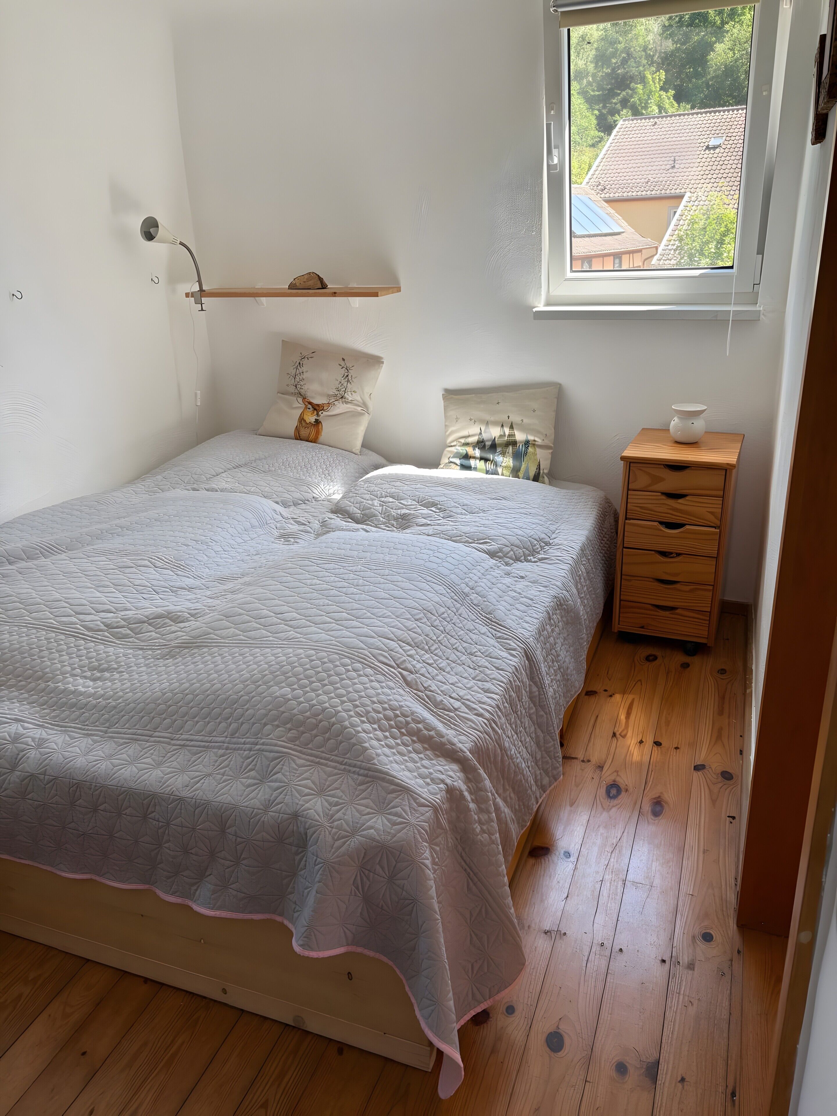 Une chambre à coucher comprenant un lit, une table de chevet, une commode, une fenêtre et une étagère fixée au mur.