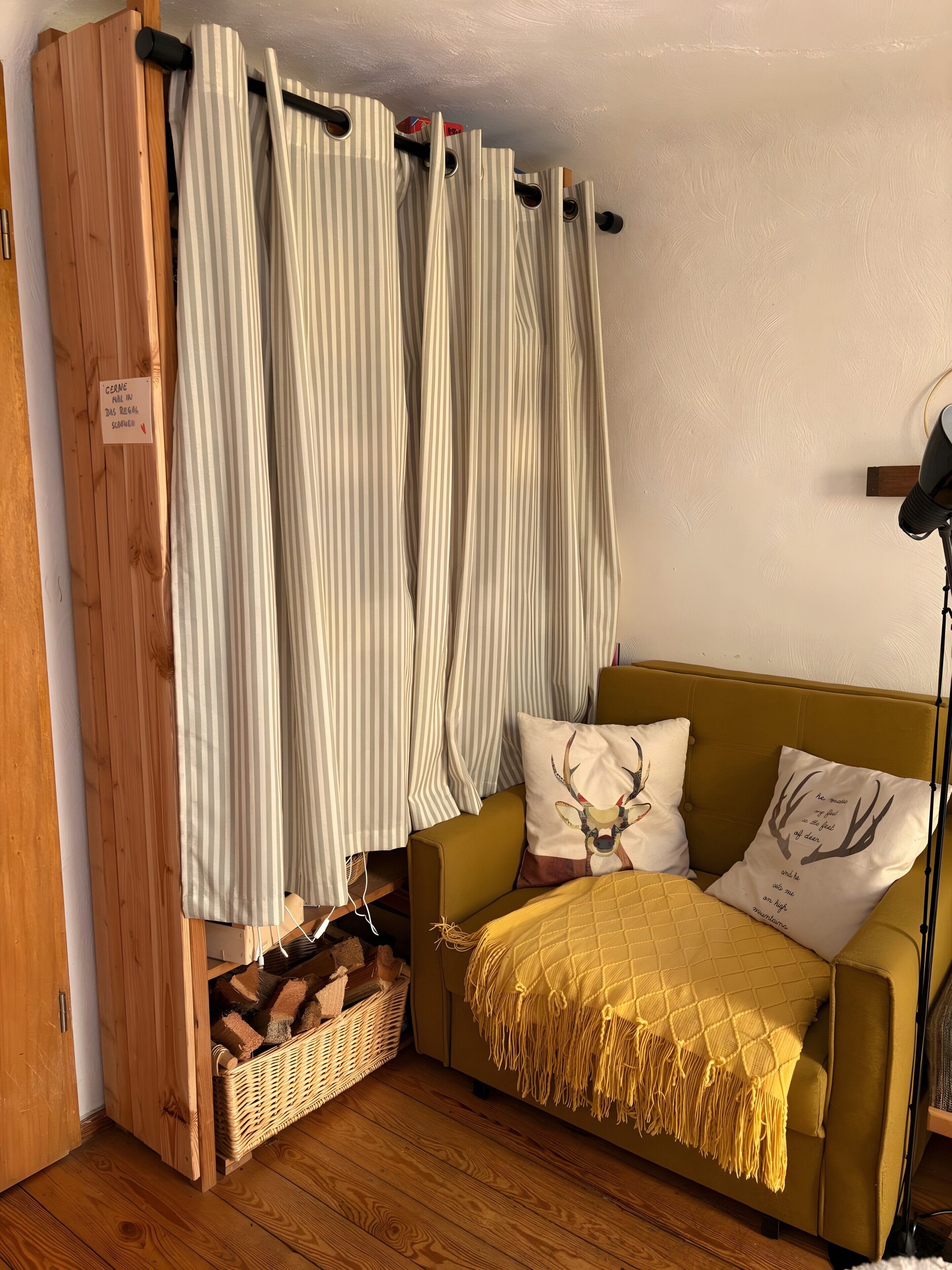 Une pièce chaleureuse avec une armoire en bois, un rideau à rayures, un canapé jaune agrémenté de coussins à motifs et un panier en osier.