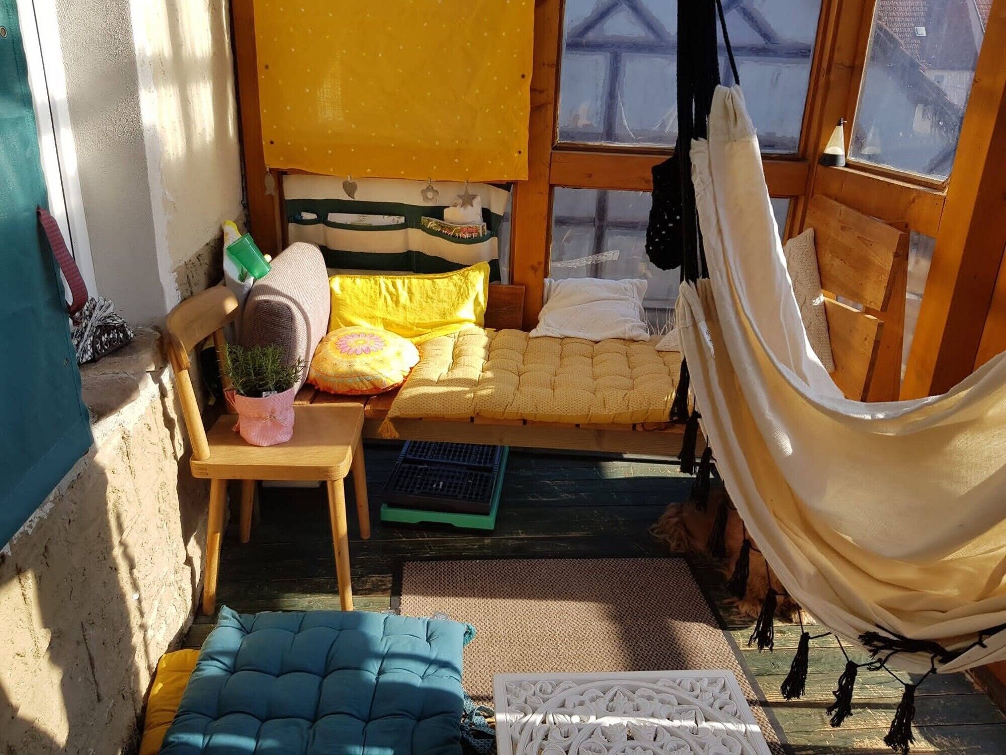 Ein gemütliches Zimmer mit einer Hängematte, einem Bett mit gelber Bettwäsche, einem kleinen Tisch mit einer Pflanze und einer blauen gepolsterten Bank.