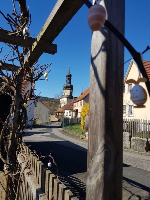 Une rue de campagne bordée d’une clôture en bois, une église dotée d’un clocher et des maisons à l’architecture traditionnelle.