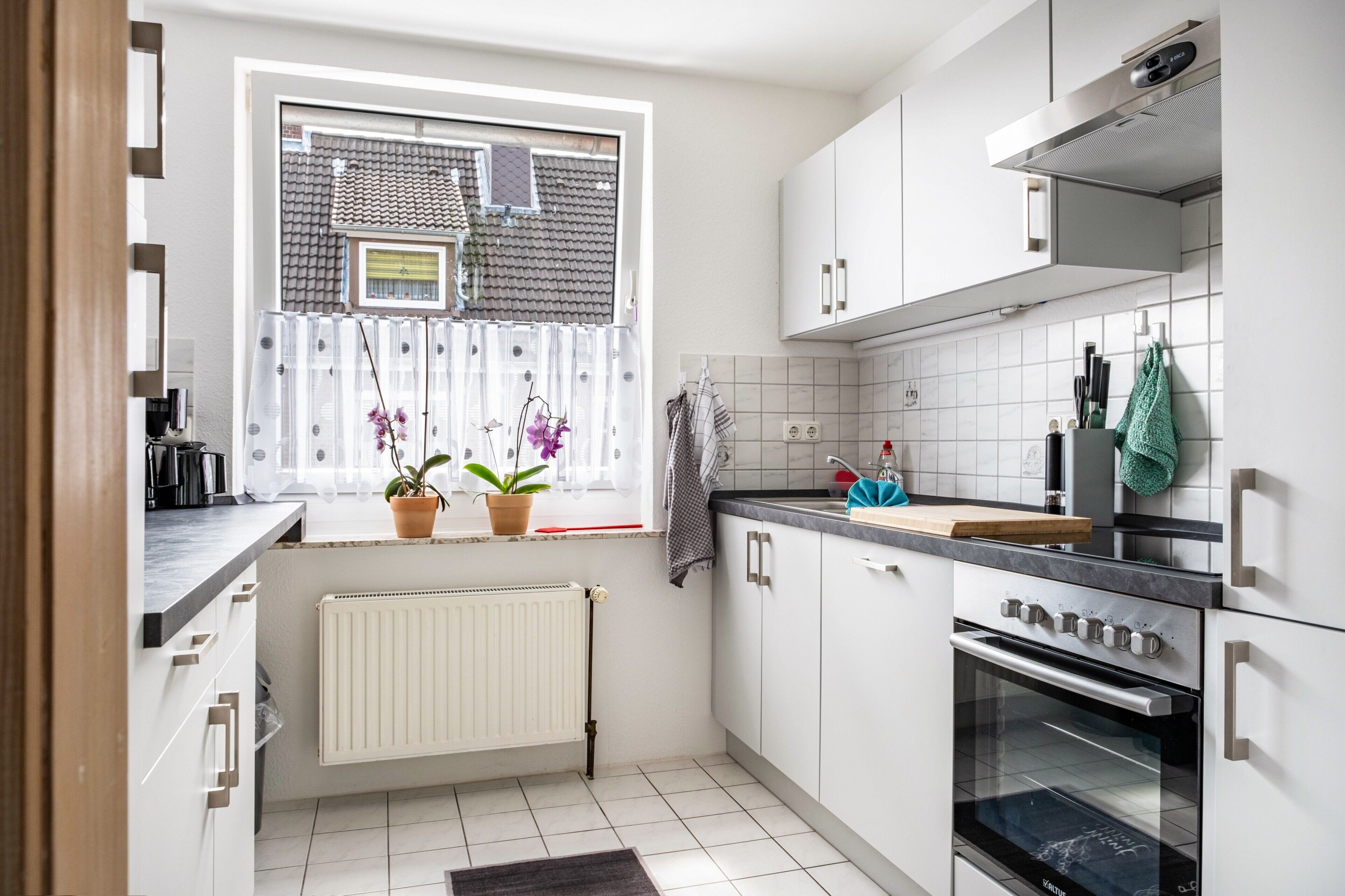 Eine moderne Küche mit weißen Schränken, einem Einbauofen und einem Fenster mit Blumentöpfen.