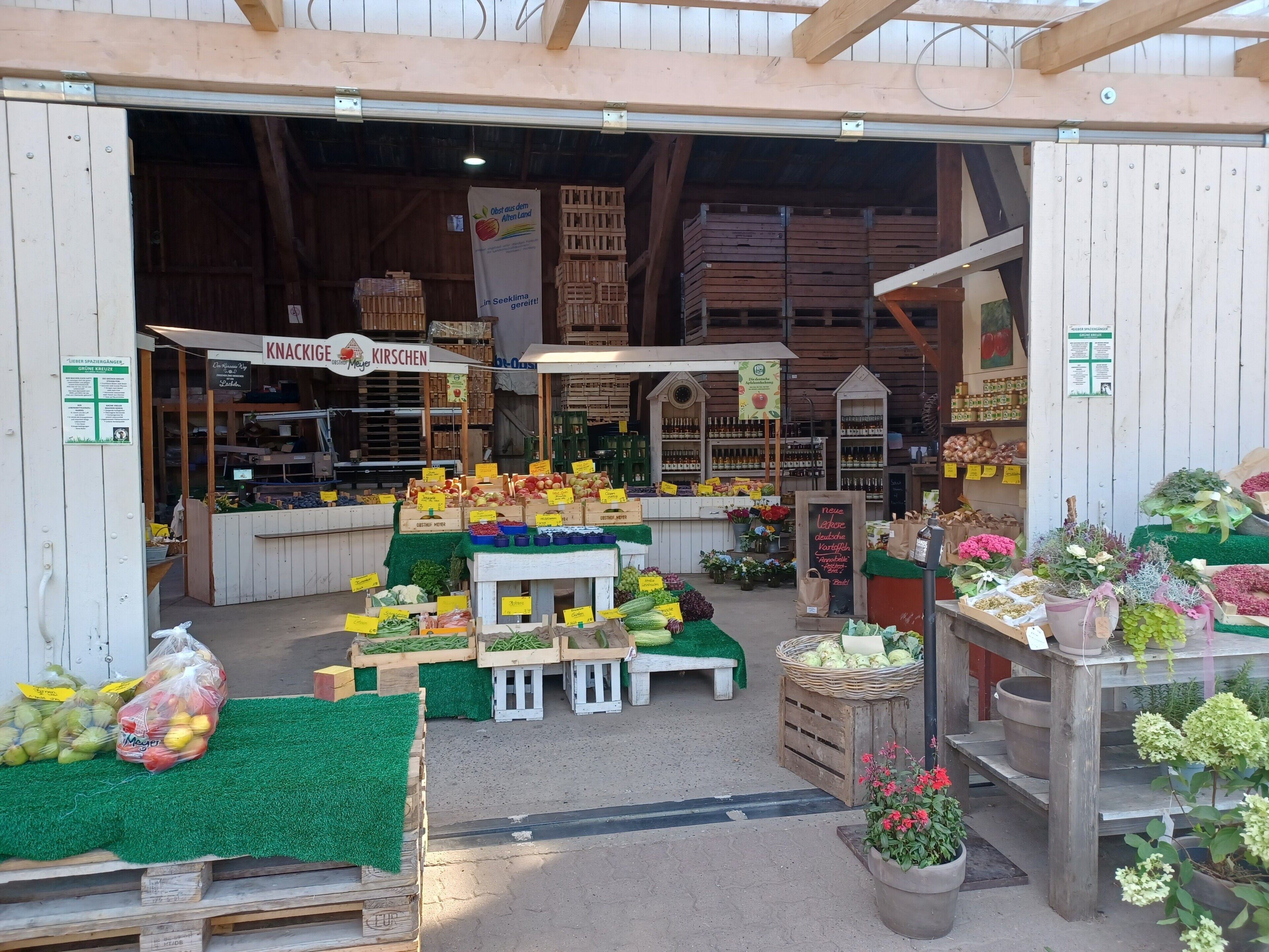 Een marktkraam met diverse soorten fruit en groenten, gepresenteerd op houten kisten en tafels.