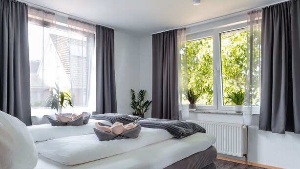 Een moderne slaapkamer met twee bedden, grijze gordijnen, een raam met uitzicht op groen en een witte radiator.