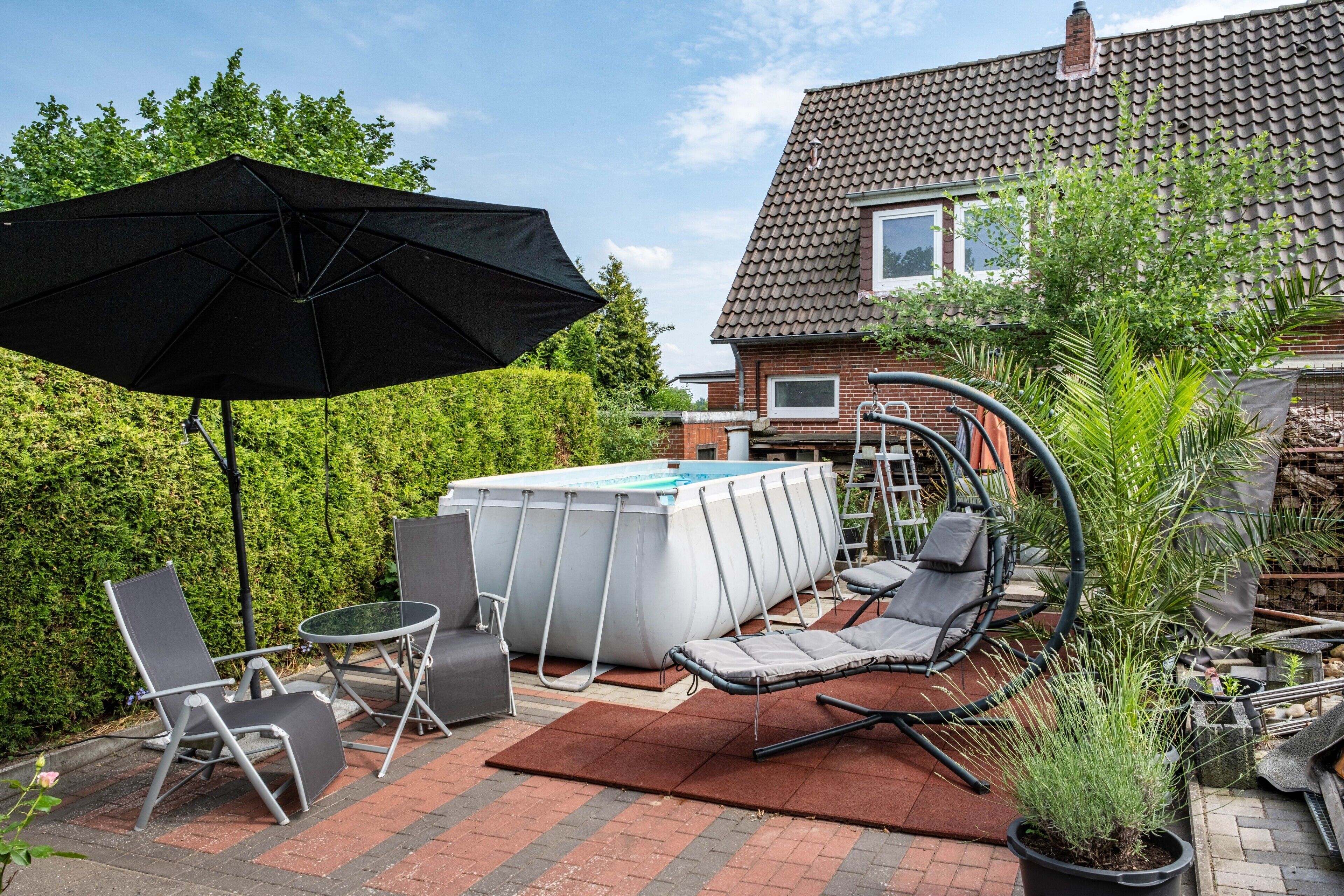 A backyard with a swimming pool, lounge chairs, a table, and an umbrella.