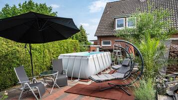 A backyard with a swimming pool, lounge chairs, a table, and an umbrella.