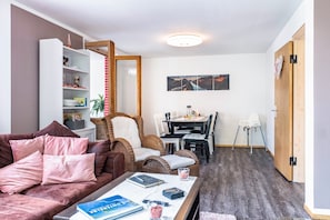 En stue med sofa, sofabord, reol, spiseplads med stole og en trædør.