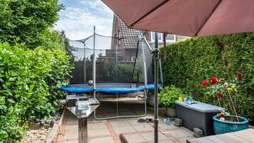 Un jardin avec un trampoline, une table et un pot de fleurs.