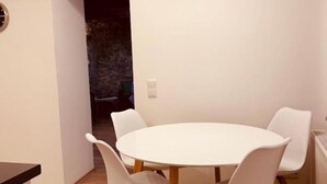 A modern dining area with a round table and four white chairs, wooden flooring, and a recessed ceiling light fixture.