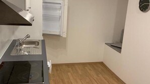 A compact kitchen with a sink, stove, and a clock on the wall.