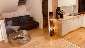 Un espace de vie compact comprenant un coin cuisine, un coin repas avec une table en verre et un coin salon confortable avec un canapé et des coussins.
