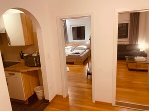 A bedroom with a bed, a bedside table, a window, and a view of a living area.