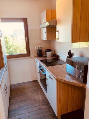 Une cuisine compacte avec des meubles en bois, un four encastré, une plaque de cuisson et une fenêtre offrant une belle vue.