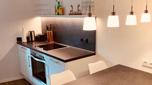 A modern kitchen with a dark countertop, white cabinets, and a wooden dining table. - Holiday Apartment "Felix Living 2" with Wi-Fi (Passau)