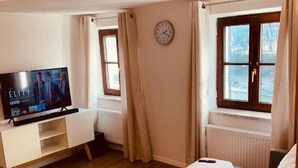 A cozy living room with a flat-screen TV, a sofa, a coffee table, and a clock on the wall. - Holiday Apartment "Felix Living 2" with Wi-Fi (Passau)