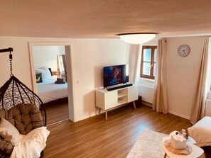 Ein gemütlicher Wohnraum mit Fernseher, einer Hängematte, einem Bett und einem Fenster.