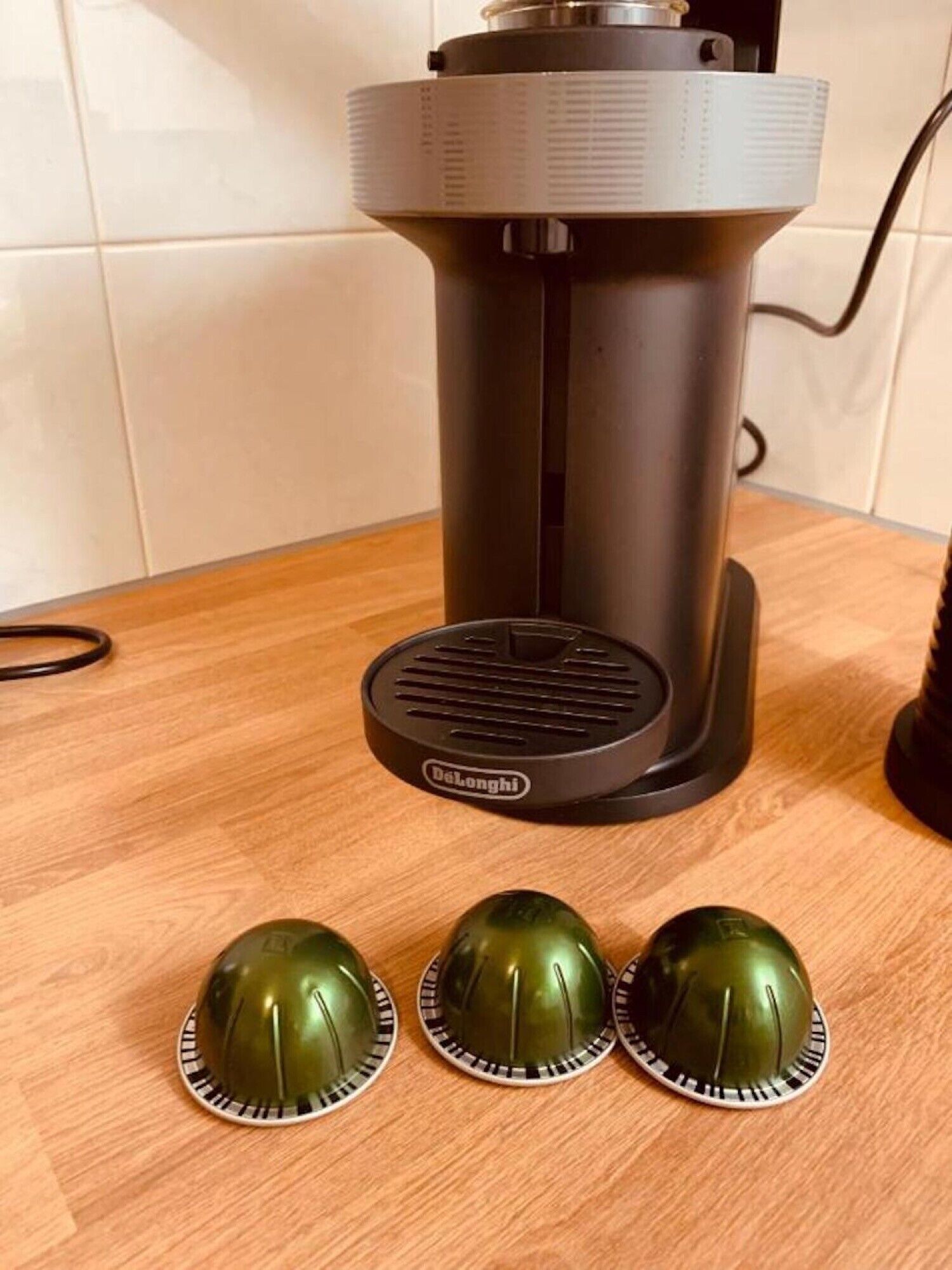 Een Delonghi elektrische waterkoker op een houten tafel, met drie groene koffiekopjes.
