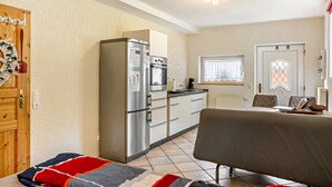 A compact kitchen with a refrigerator, oven, and a dining area with a table and chairs. - Studio Apartment "Belroki Ranch" with Sauna, Terrace, and Garden (Waldeck)